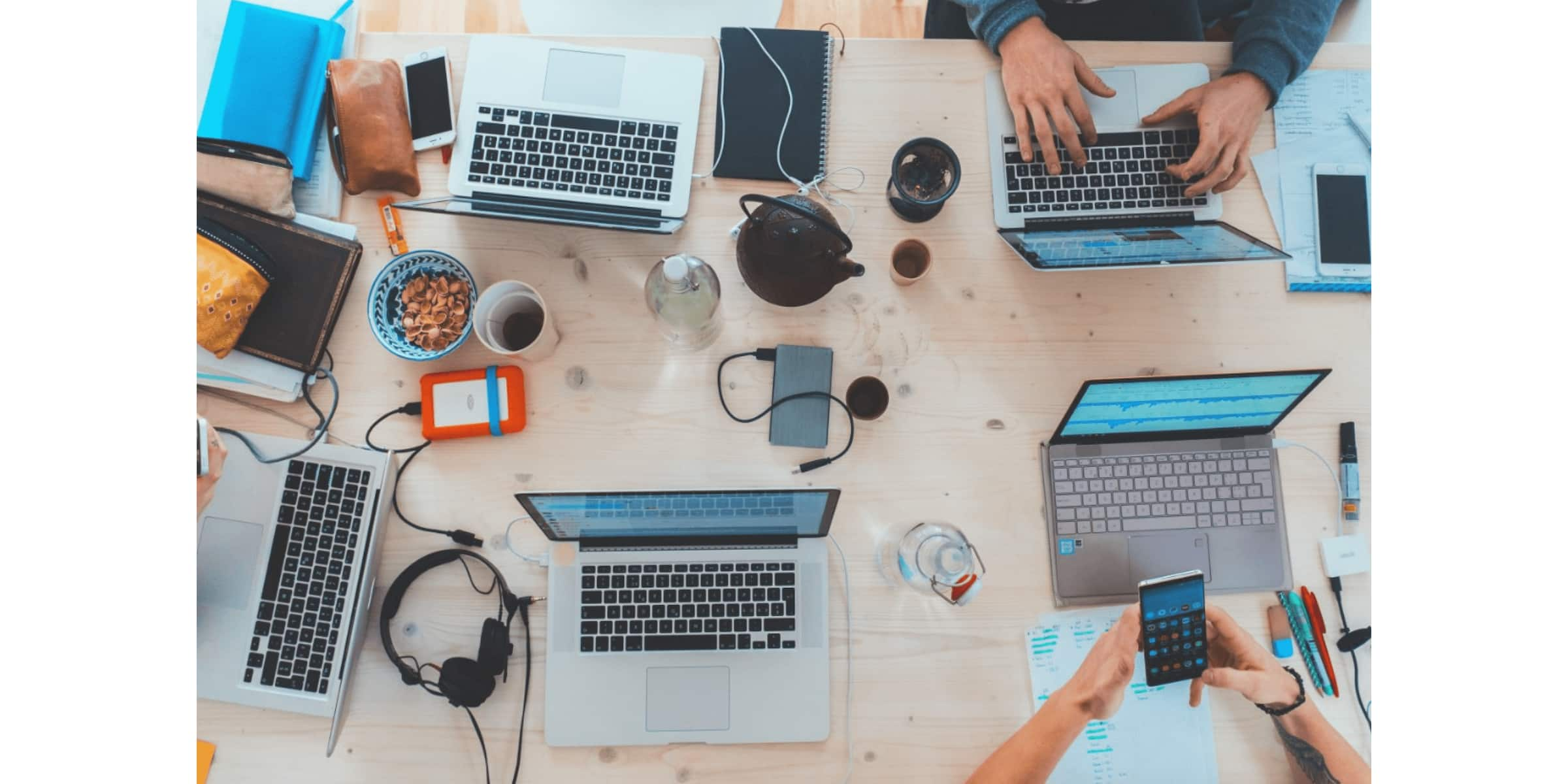 Members of a product team work together, with their laptops, mobile phones and other devices scattered across a table.