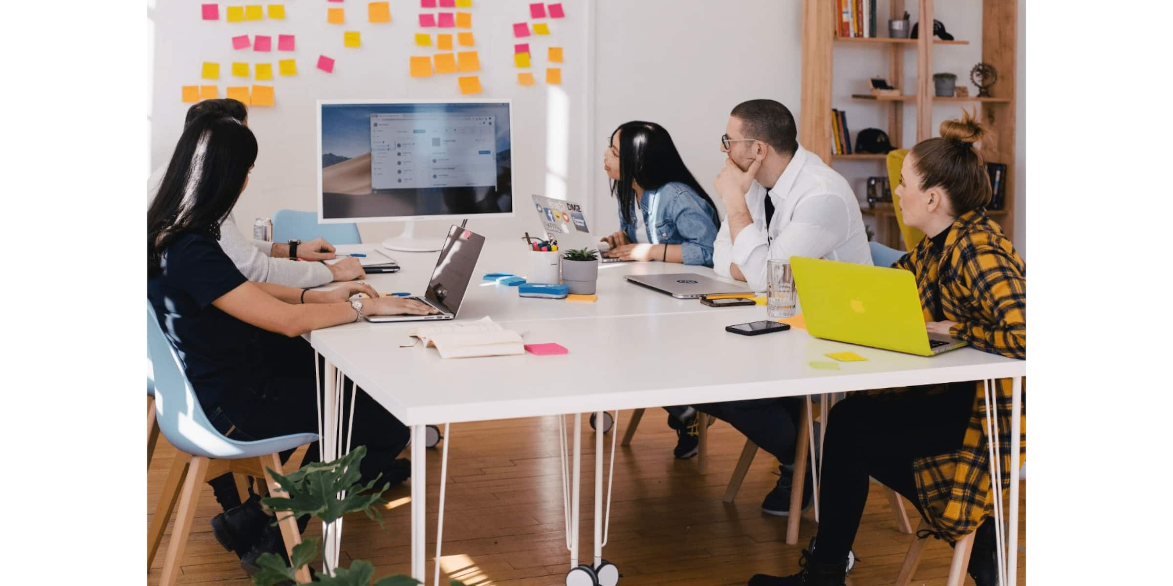 Members of a product team sit around a table and view a computer screen displaying the progress of their project.