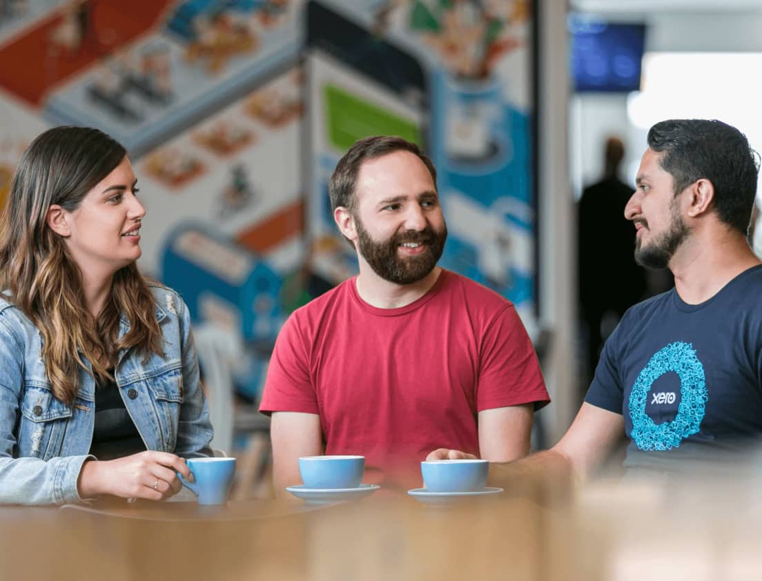 Two Xero accountants chat to a Xero team member over a cup of coffee.
