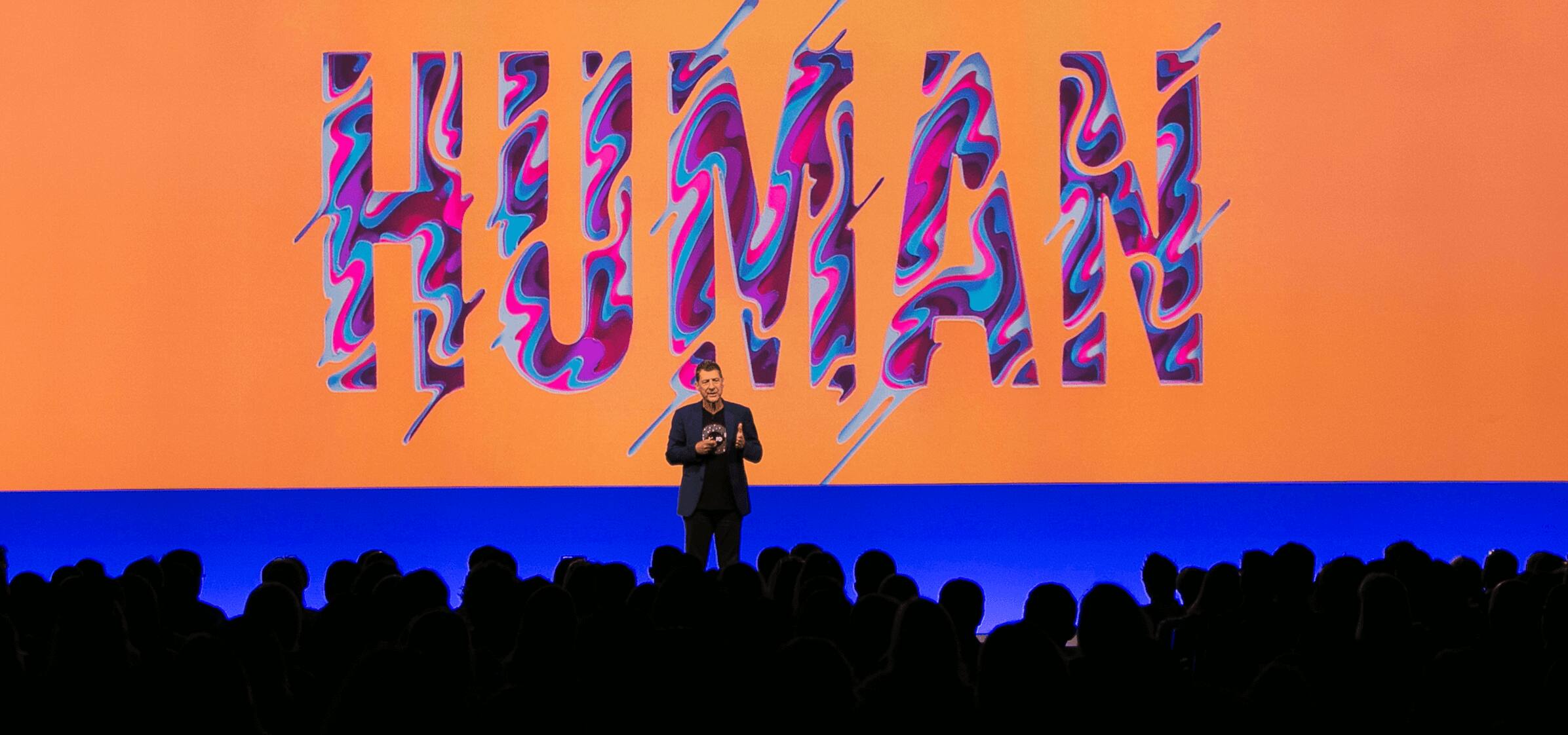 Xero CEO Steve Vamos talks to a large audience with a background displaying the word ‘Human’ in large pink letters behind him