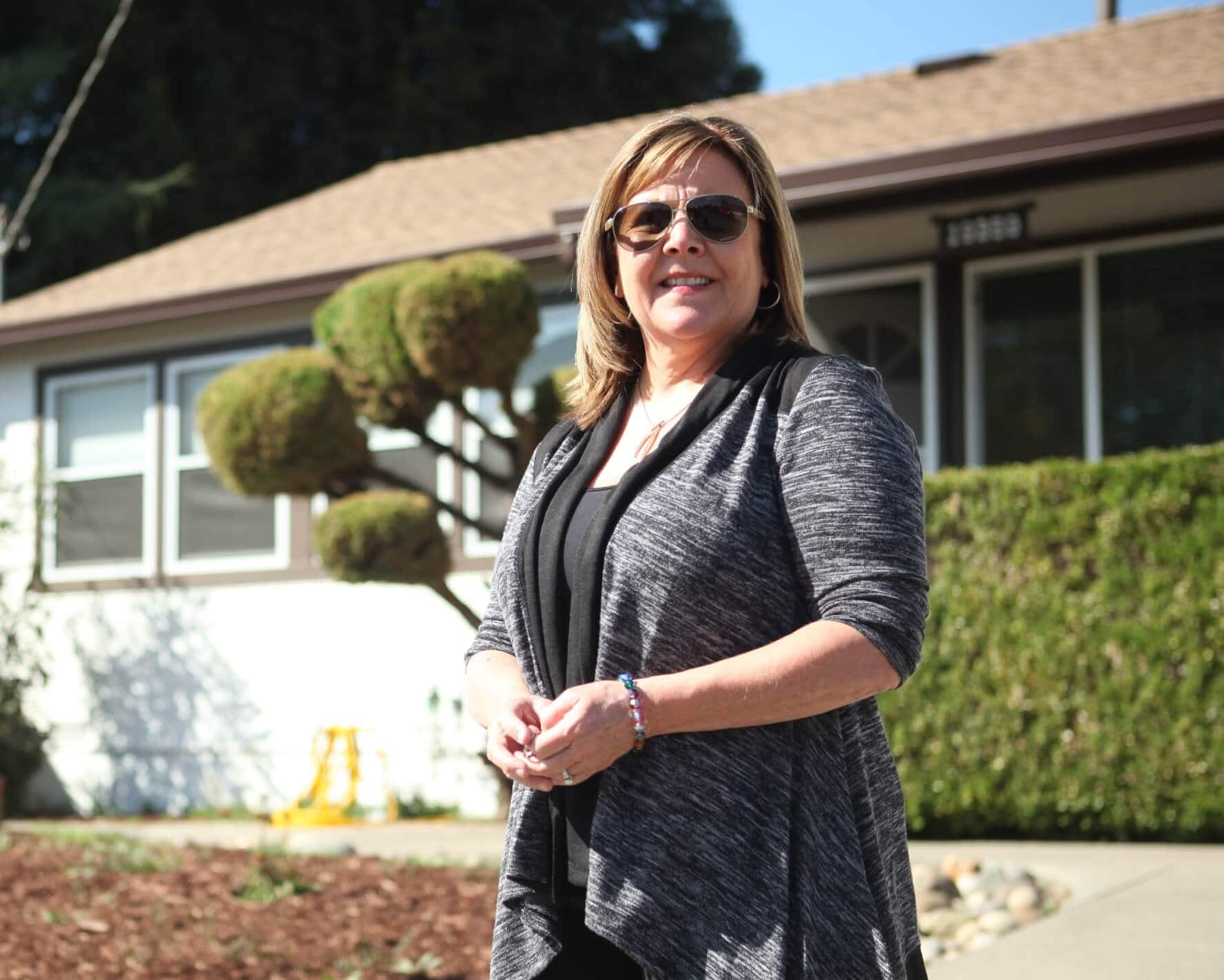 A real estate agent stands in front of a house-for-sale sign