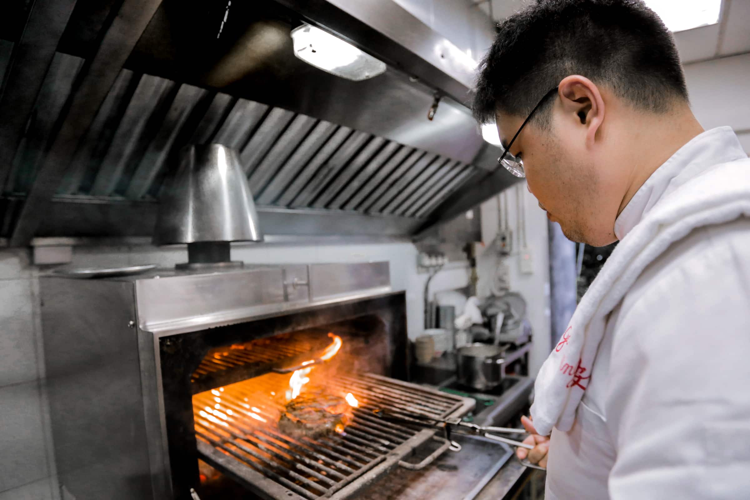A chef flame-grilling meat in a kitchen.