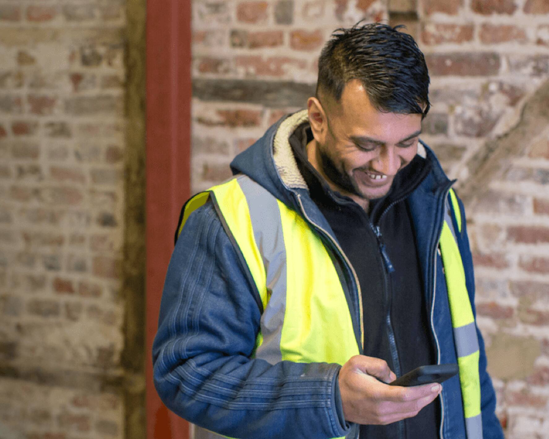 Hitesh, a construction worker, who is wearing high-visibility clothing uses construction accounting software on his mobile.