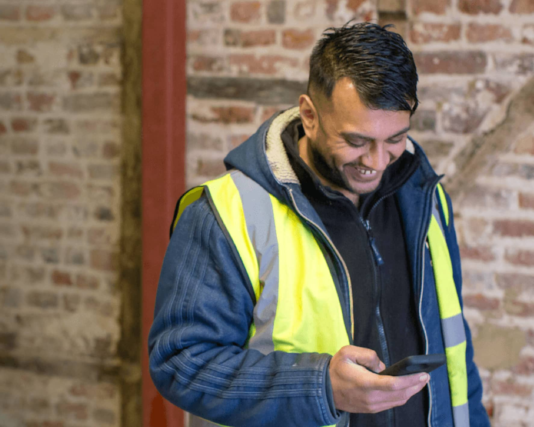 A construction worker wearing high-visibility clothing checks a mobile phone