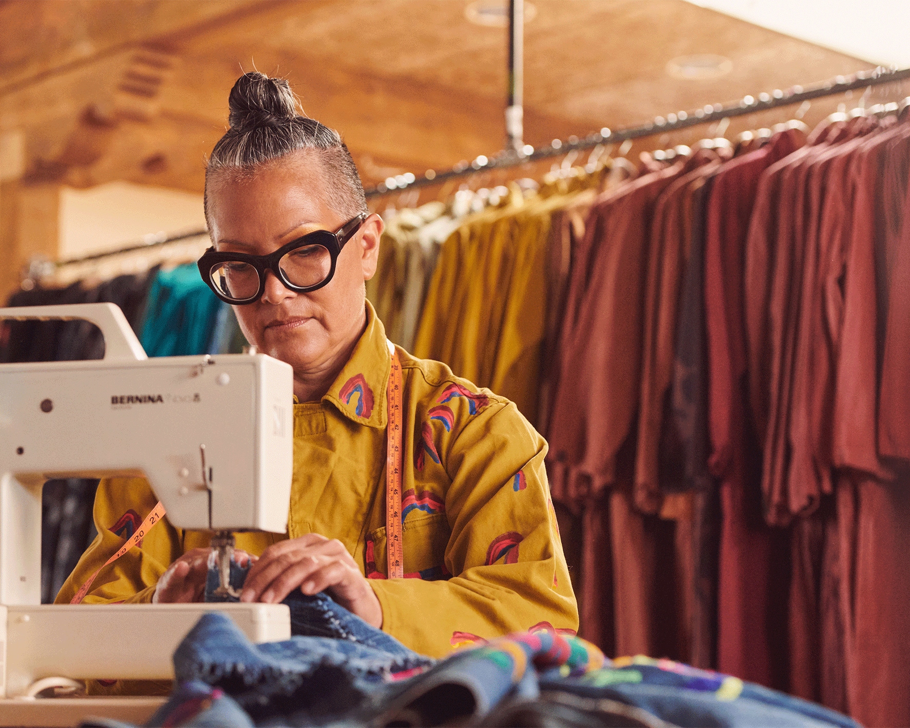 A person sewing next to full racks of garments