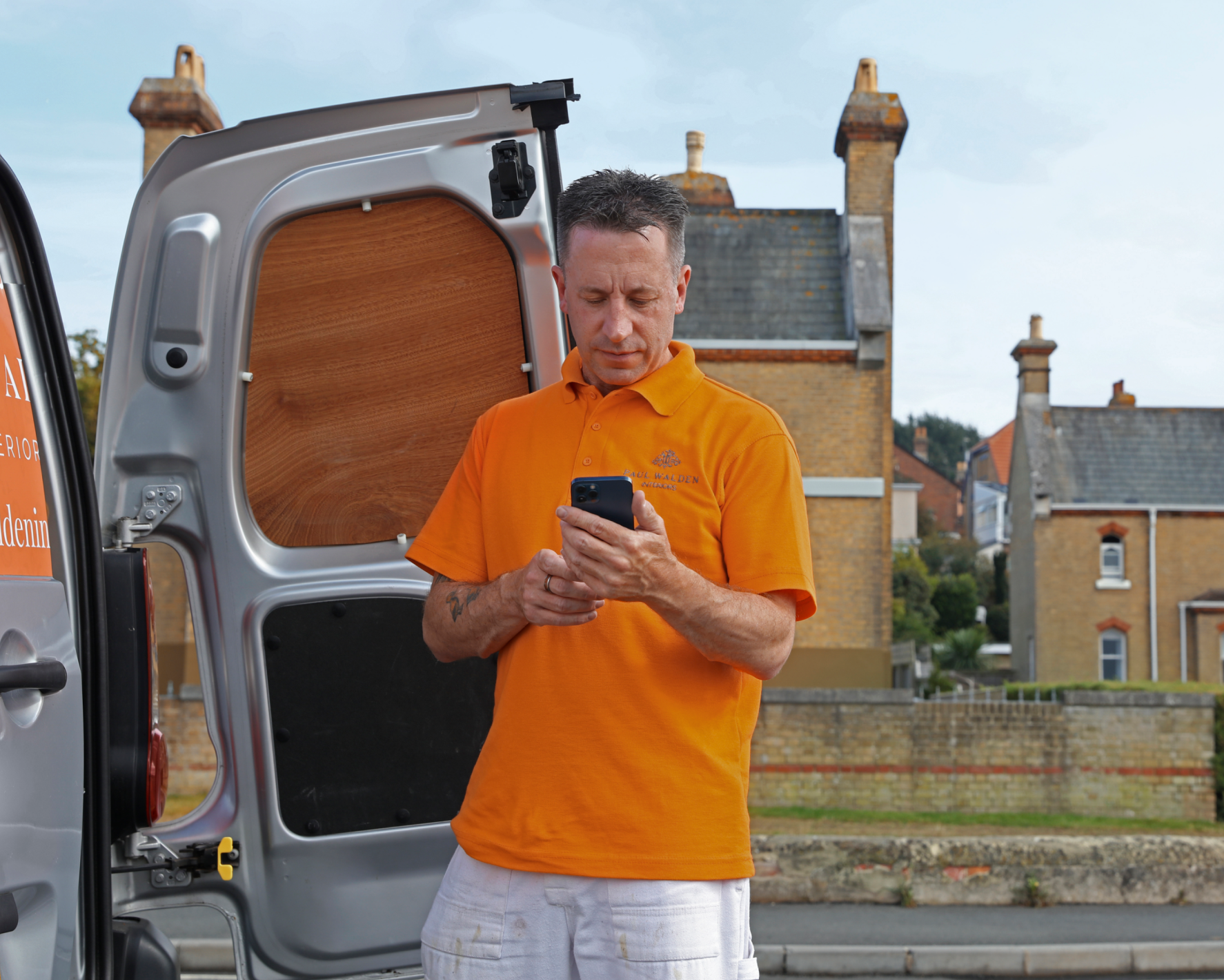 A tradesperson checking a phone next to a van