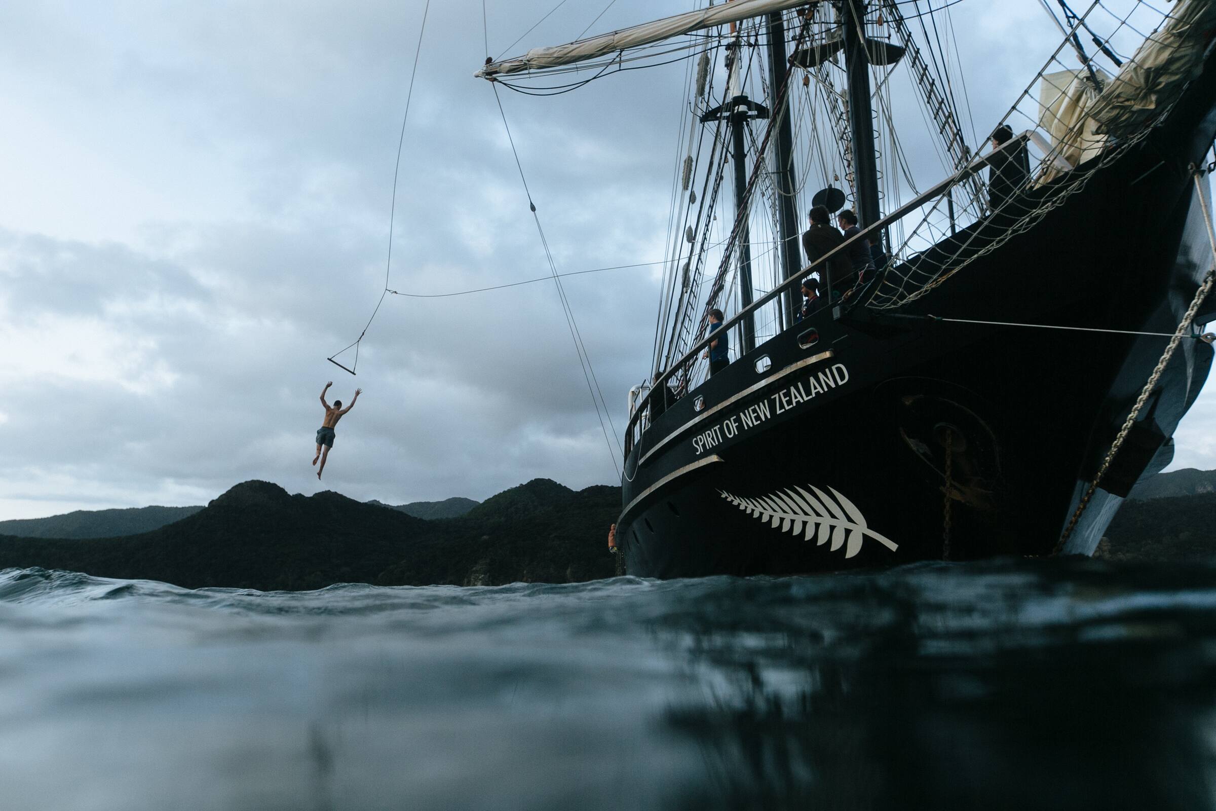Boy swinging off the Spirit of adventure ship into the ocean