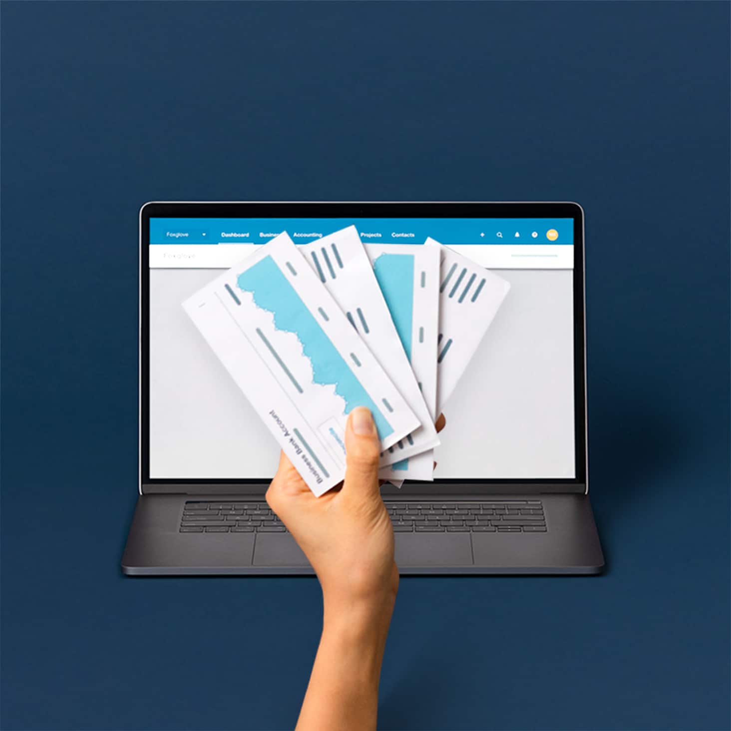 A hand holding cards with cash flow charts, in front of a laptop