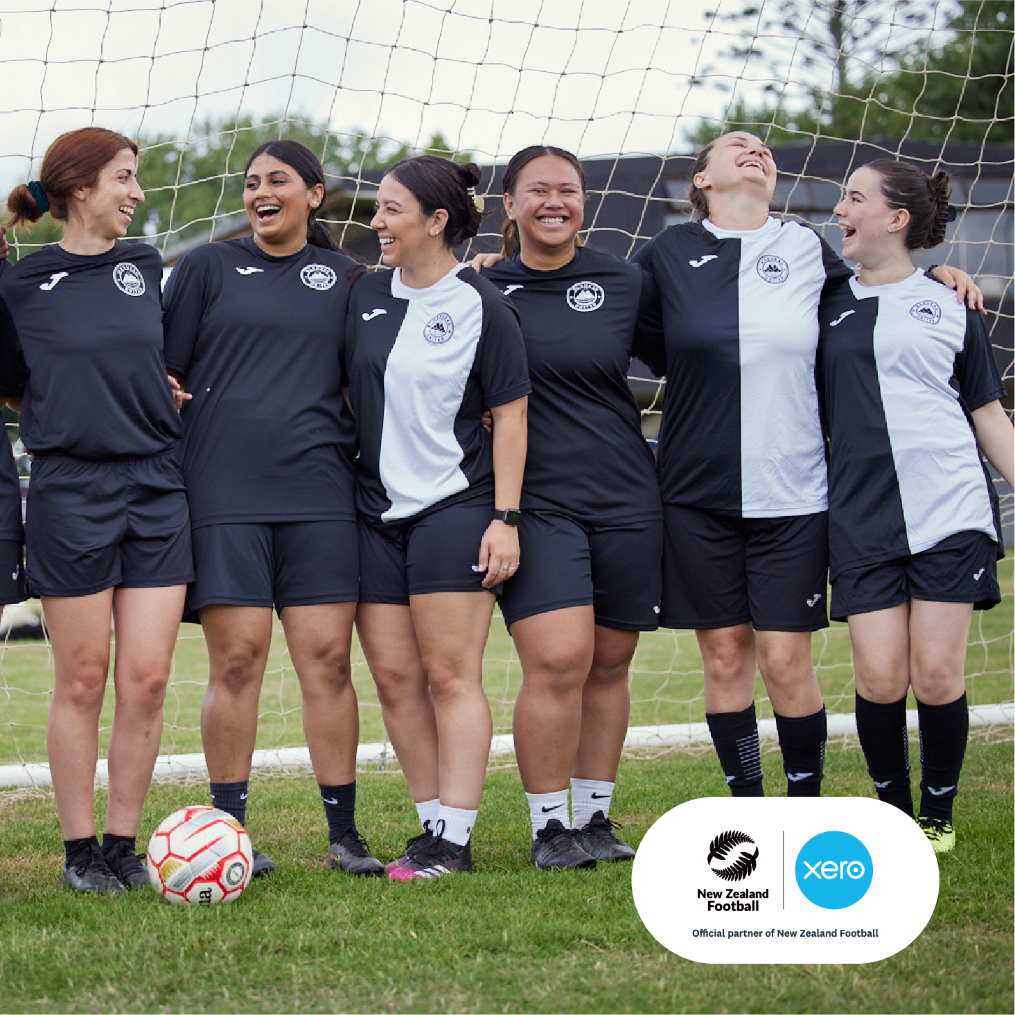 Women players from Manukau United FC stand together in front of a football goal, smiling to camera