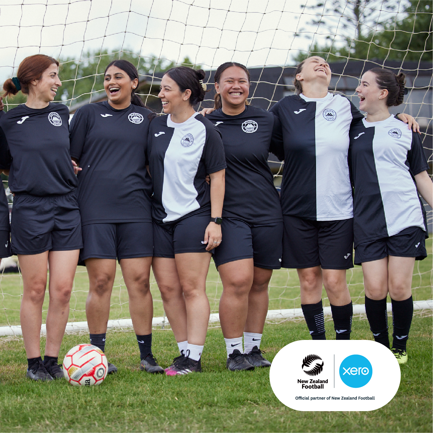 Women players from Manukau United FC stand together in front of a football goal, smiling to camera.