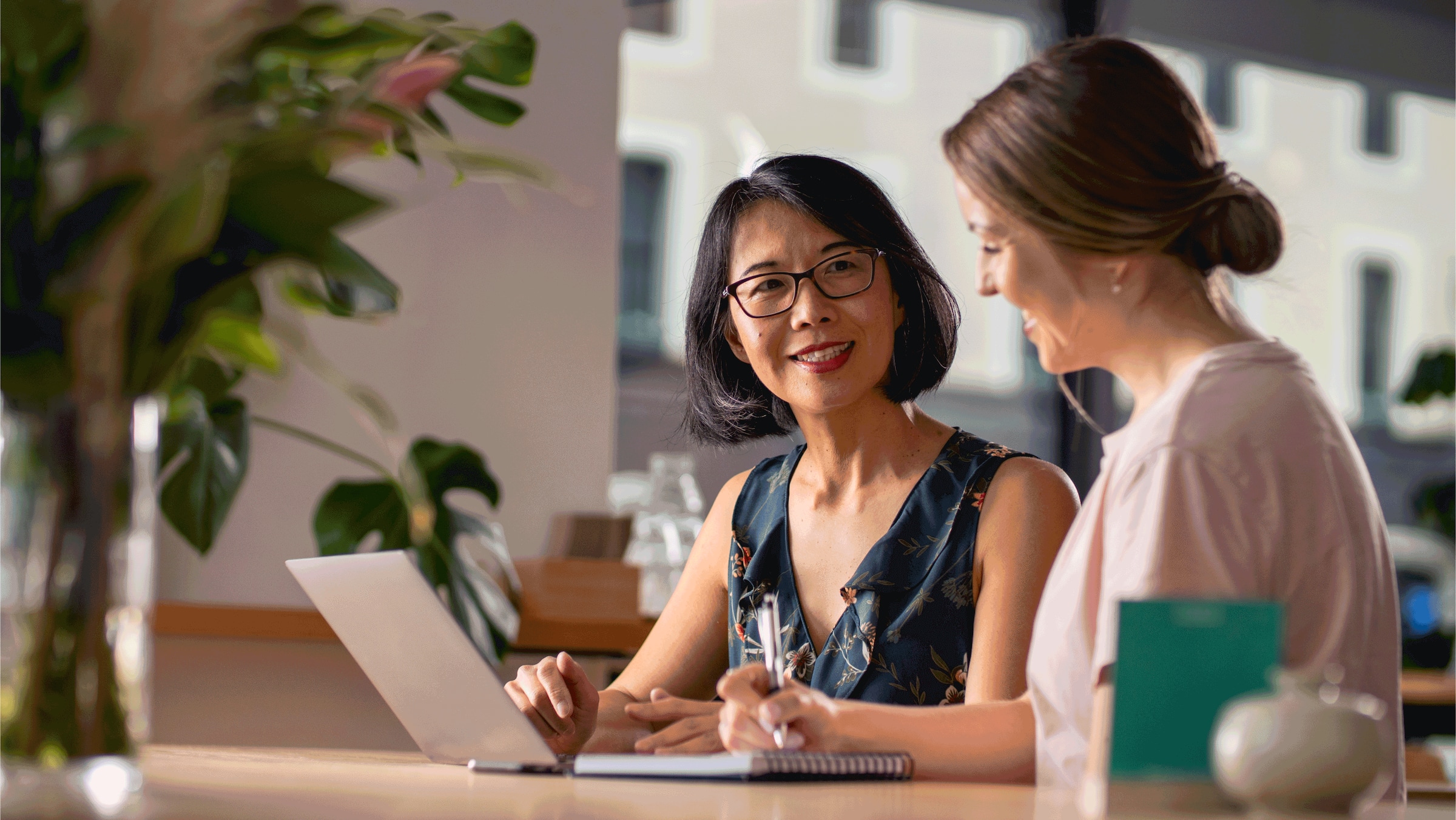 Two people standing at a desk looking at a laptop and talking to each other.