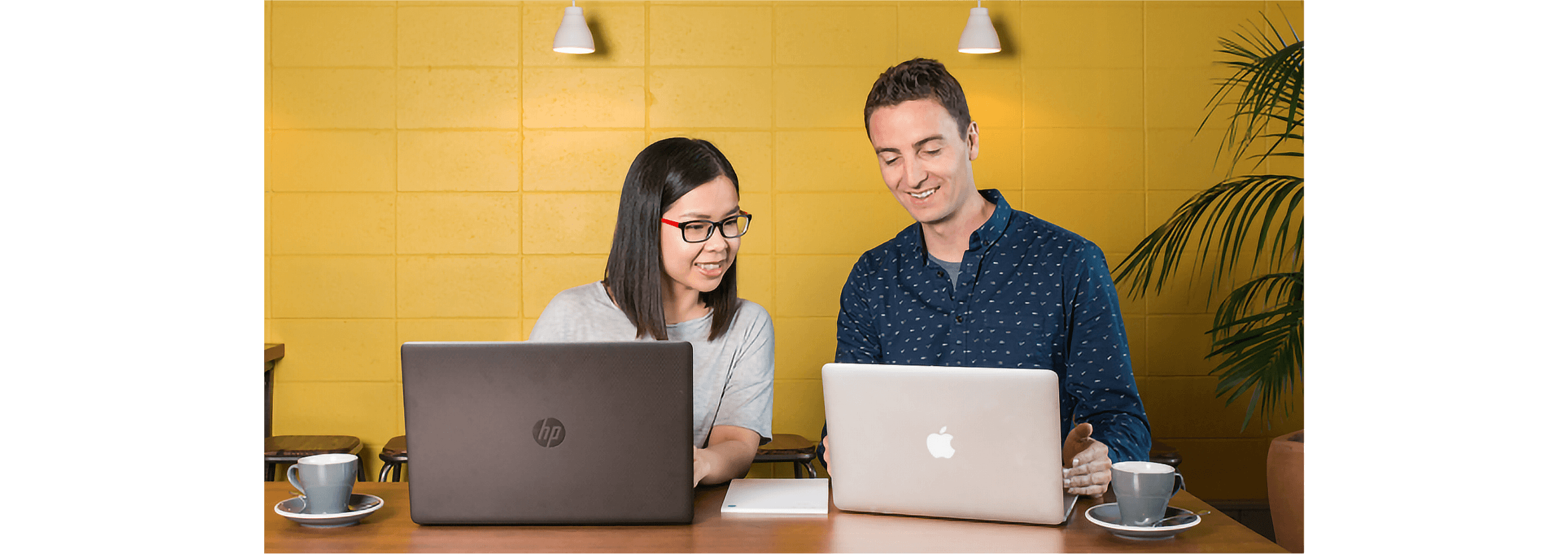Two business owners at a table with their laptop computers check Xero’s industry performance reports.