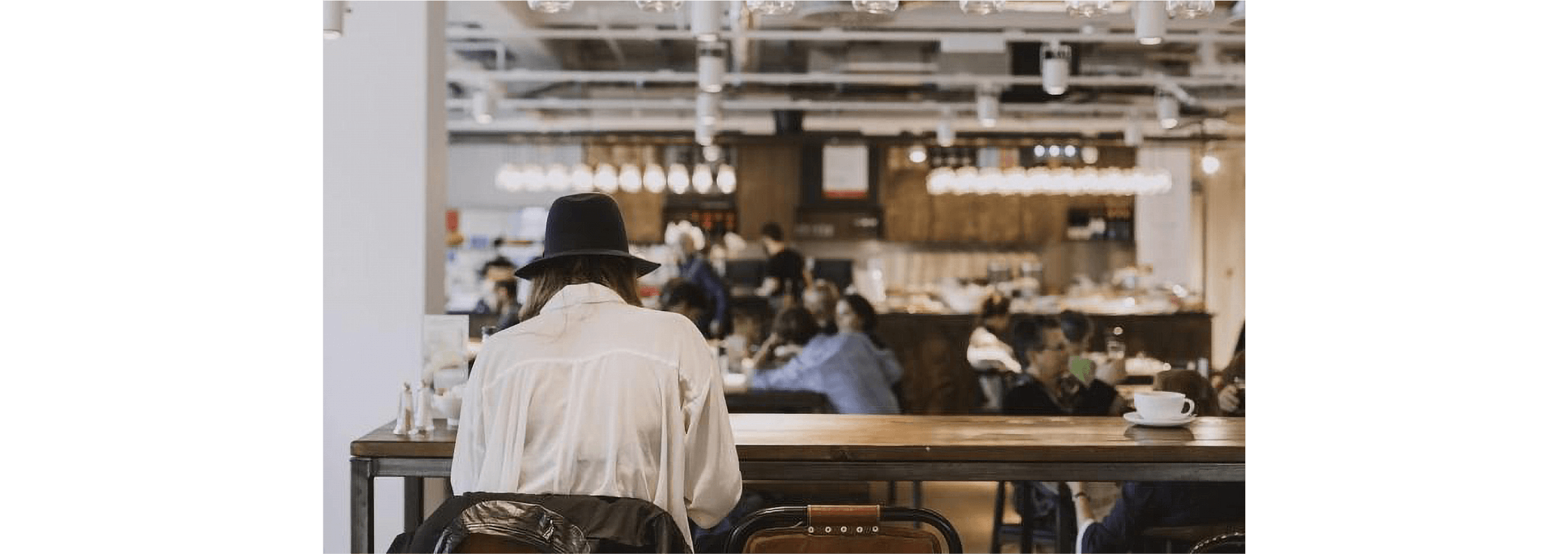 A small business owner relaxes at a table in a cafe with their back to the camera.