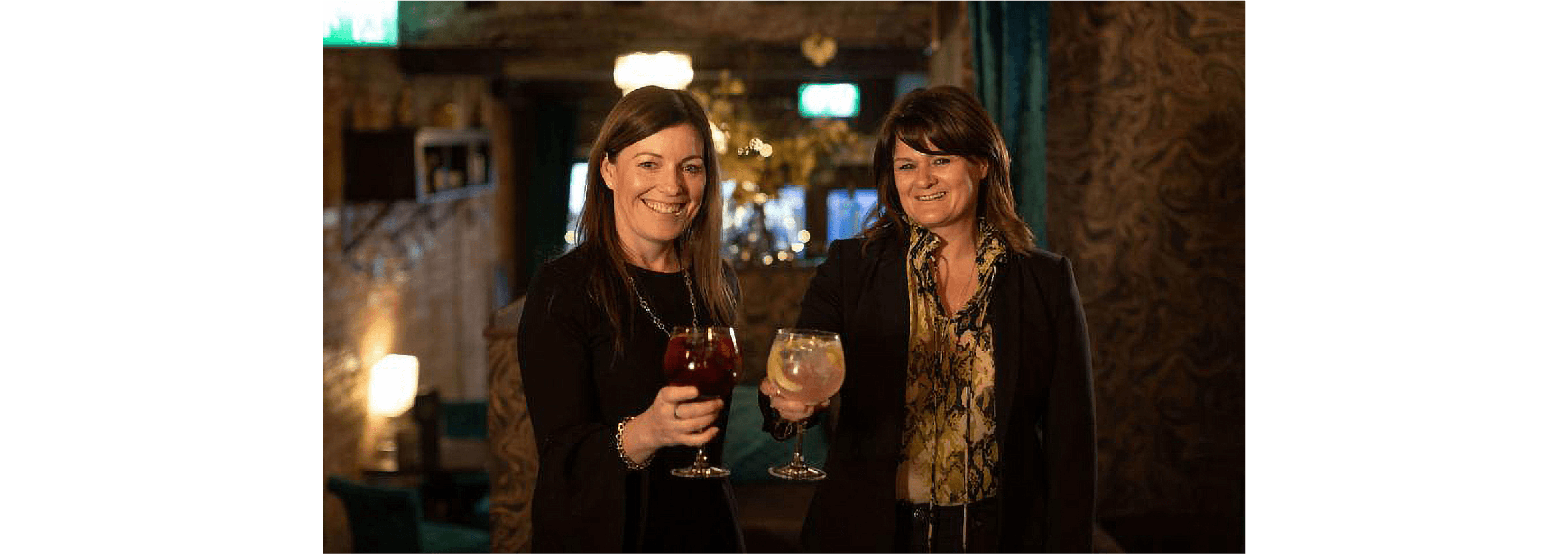 Two small business owners raise their glasses to each other at a restaurant.