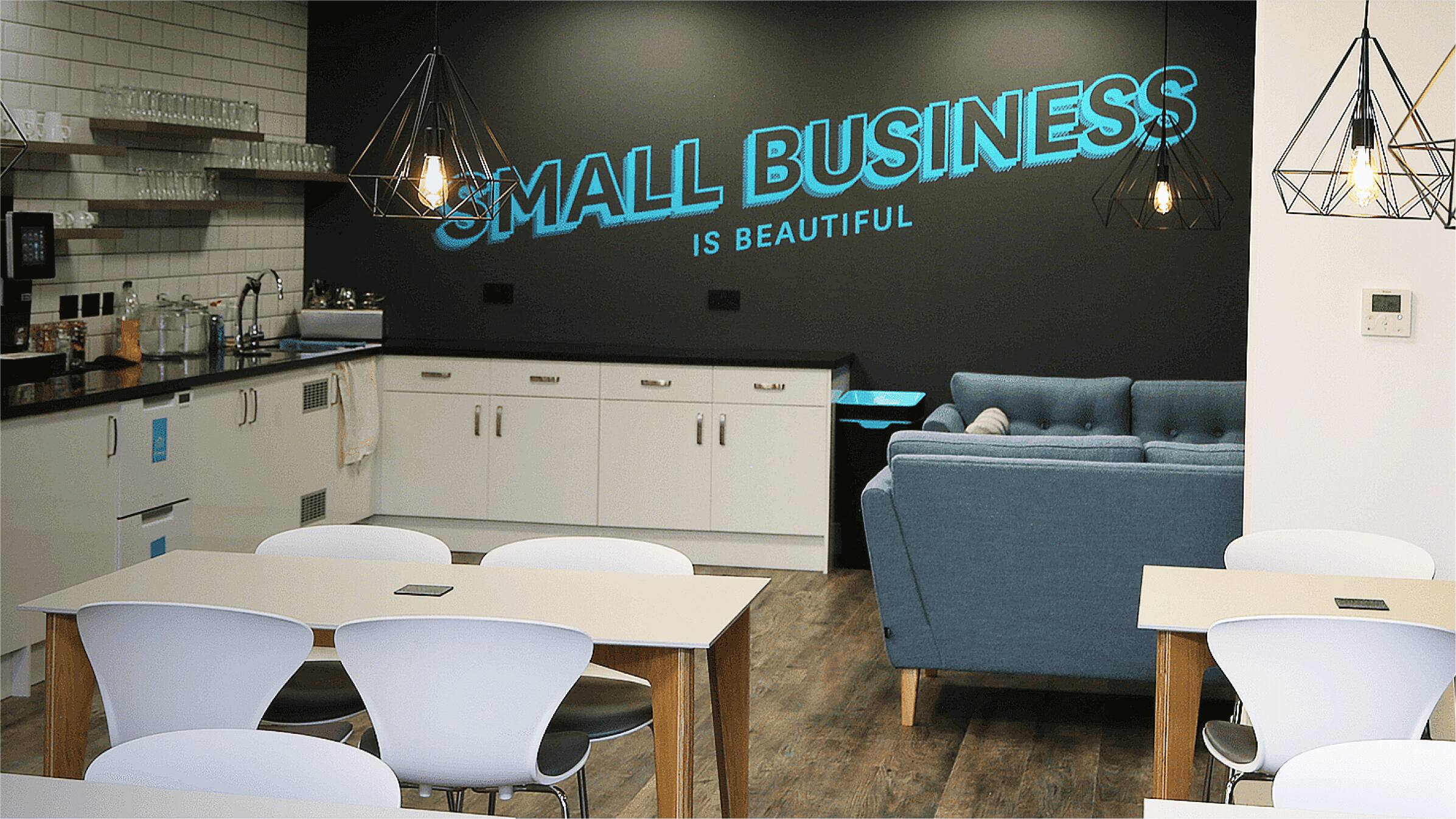 An office kitchen and dining area with ‘Small business is beautiful’ in large lettering painted on the wall.