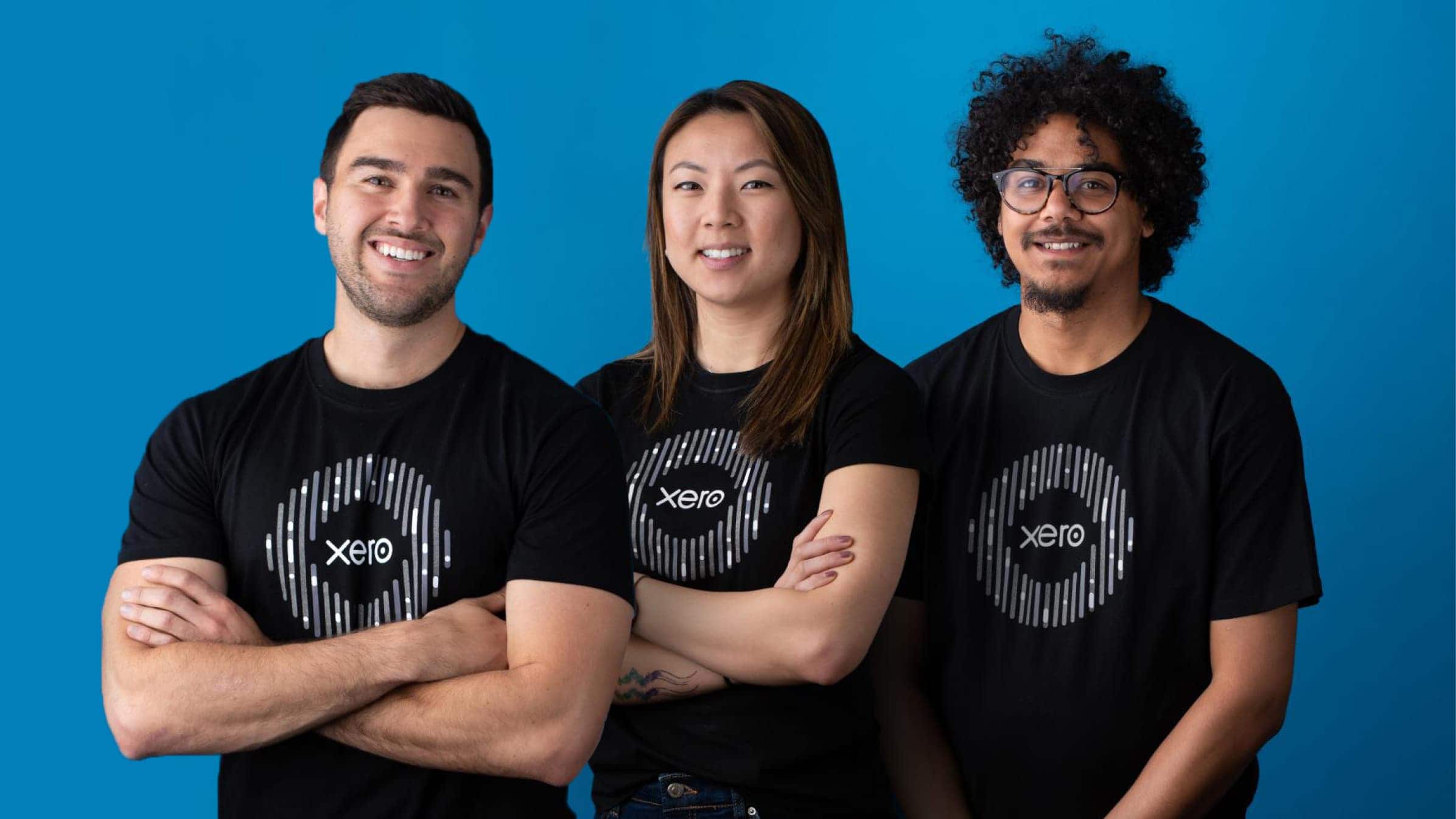 Three Xero team members standing with their arms folded wearing Xero branded back t-shirts.