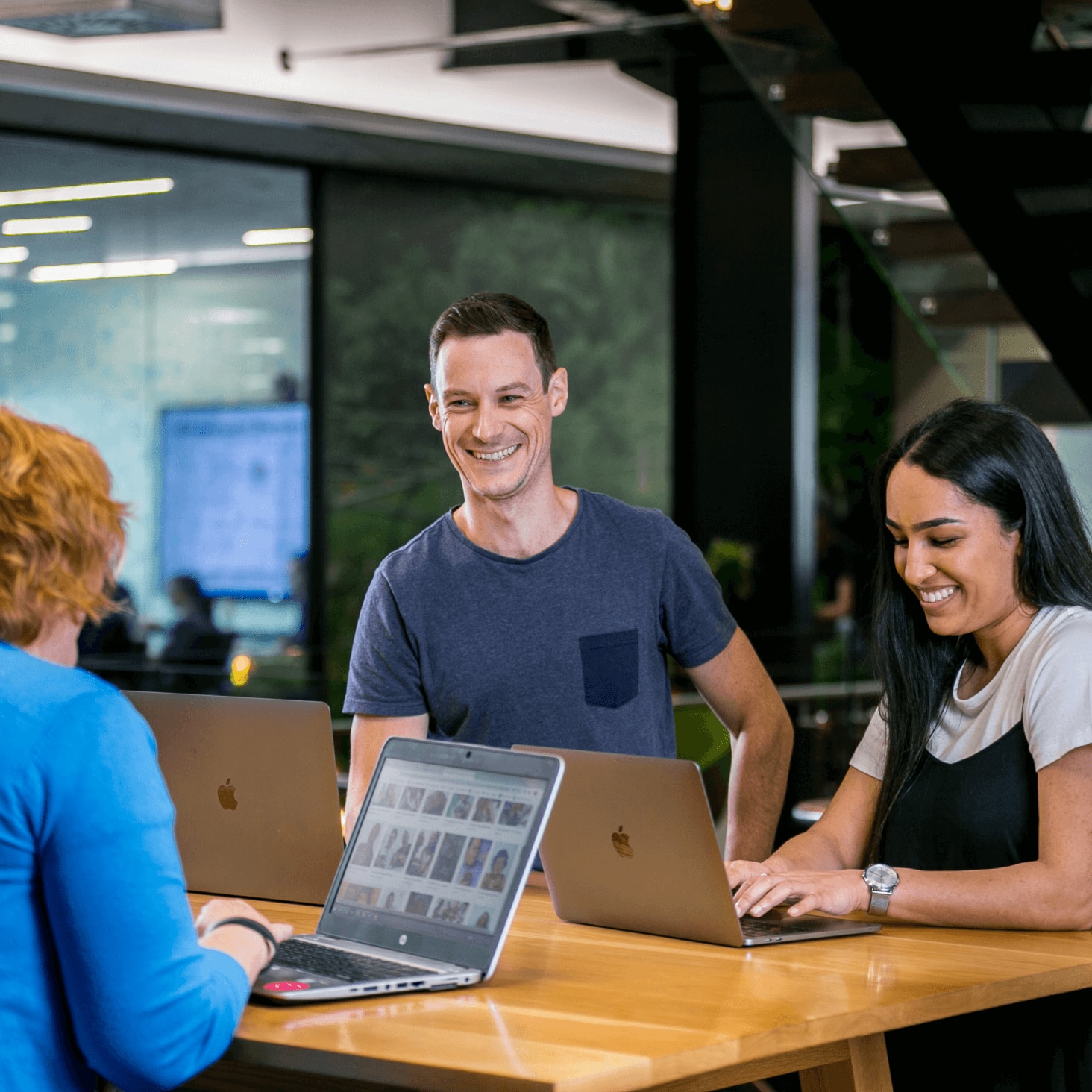 Three Xero employees with open laptops work together at a coffee table in a breakout area.