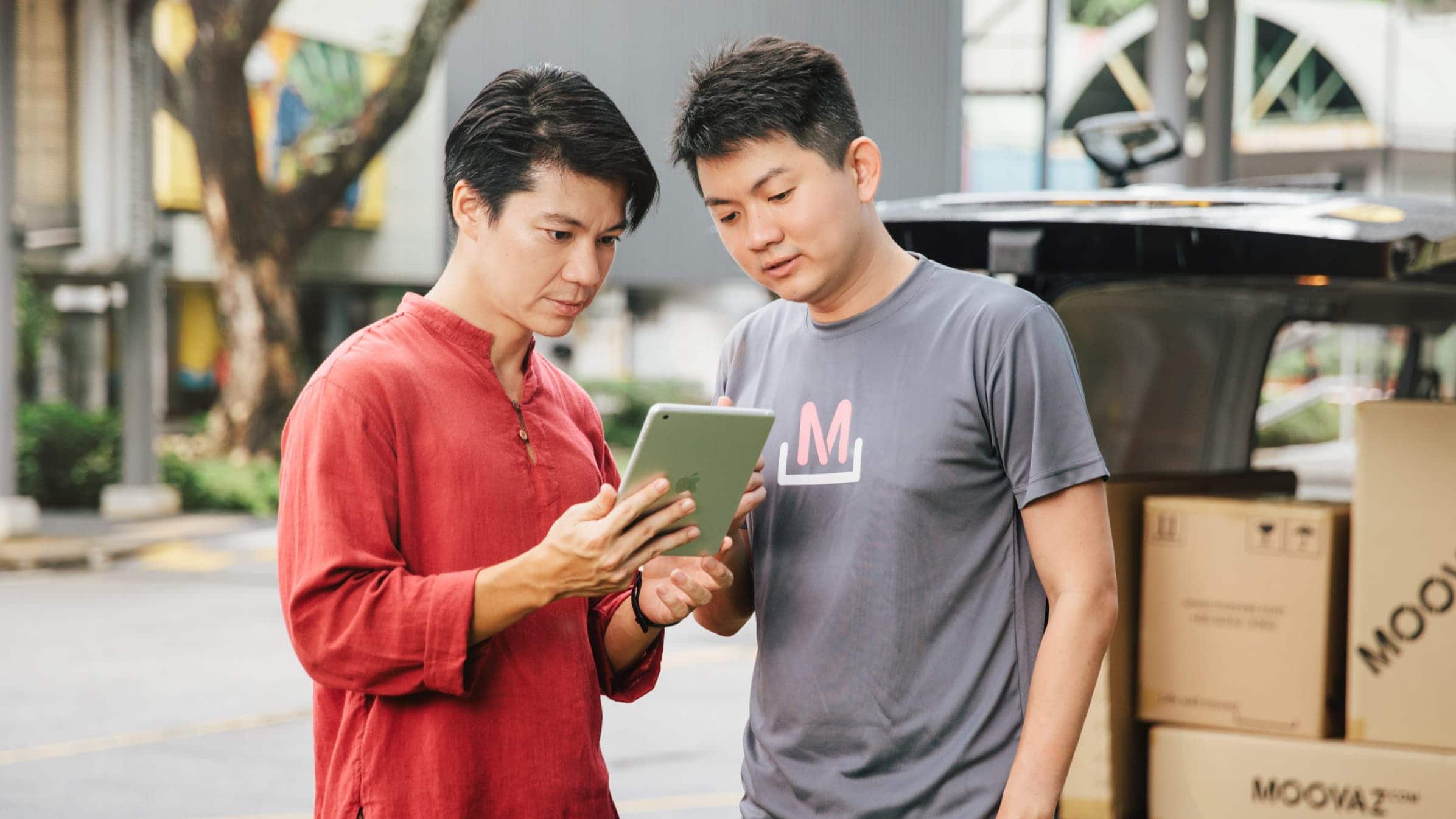 Junxian Lee, Co-founder and CEO of Moovaz, showing a tablet device to a colleague while standing beside a moving van.