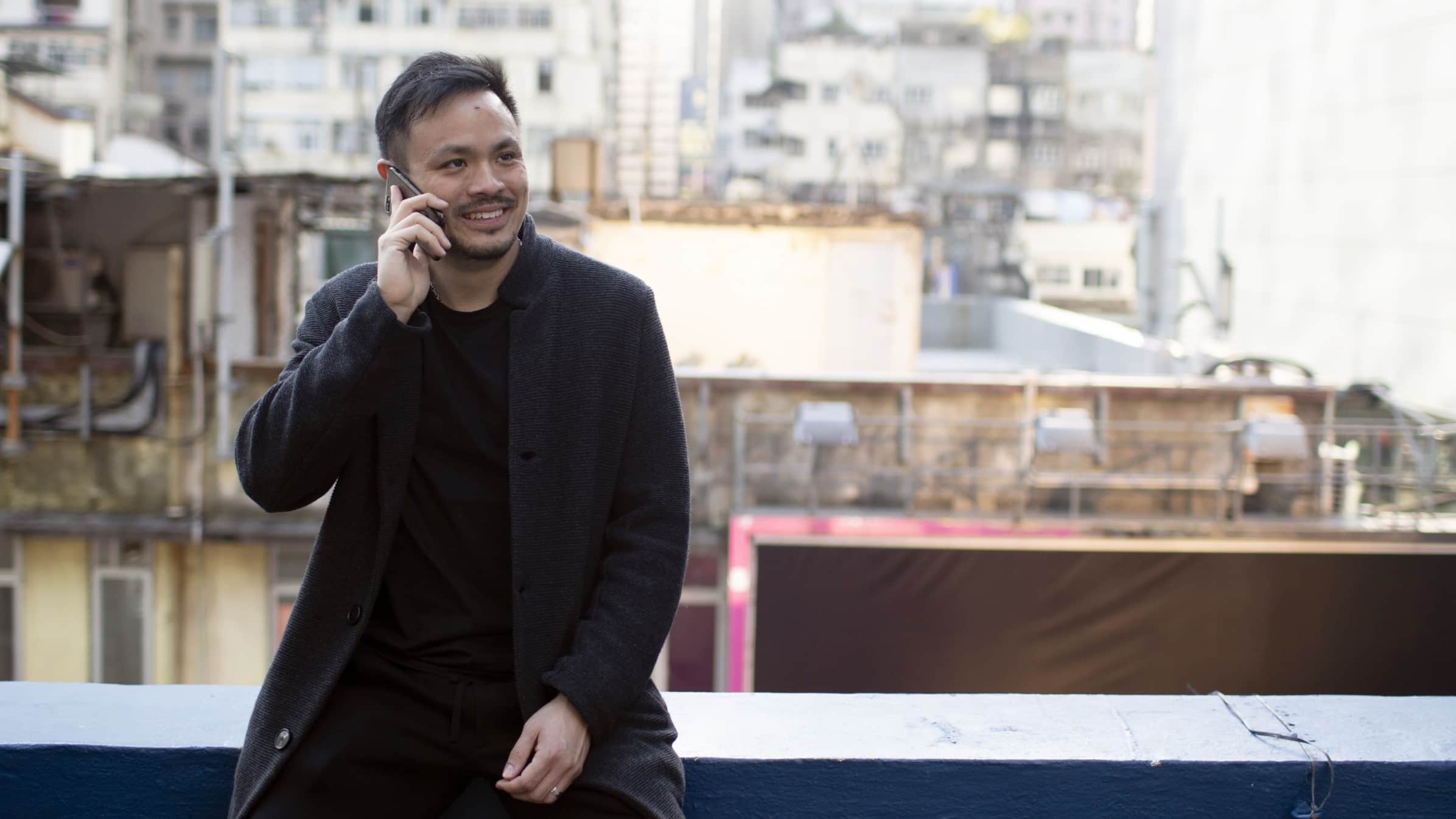 Joe Jun Liao, co-founder of SLEEP, sitting on a rooftop balcony on the phone. 